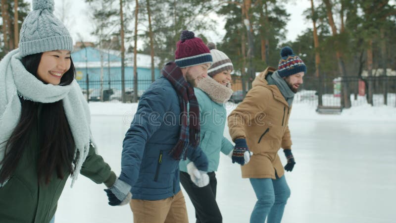 Αργή κίνηση ευτυχισμένων φίλων παγοδρομία στο πάρκο κρατώντας χέρια τη χειμερινή ημέρα