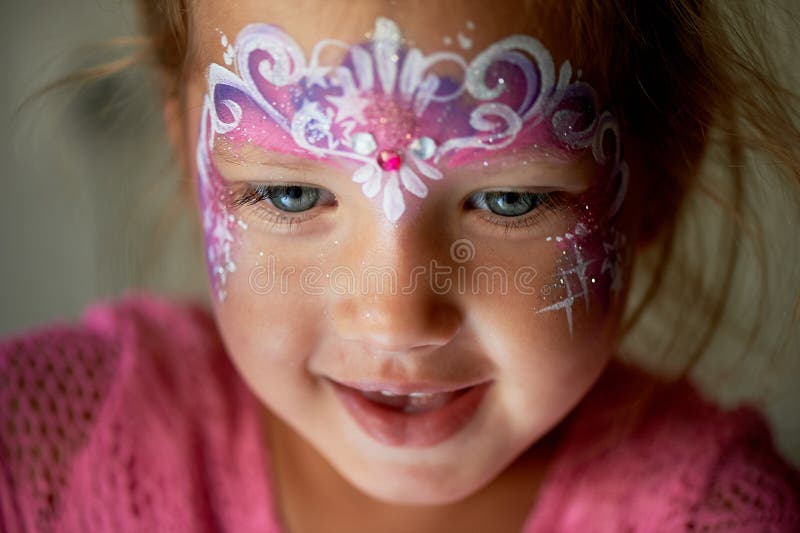 Pretty exciting blue-eyed girl of 2 years with a pink face painting. Pretty exciting blue-eyed girl of 2 years with a pink face painting