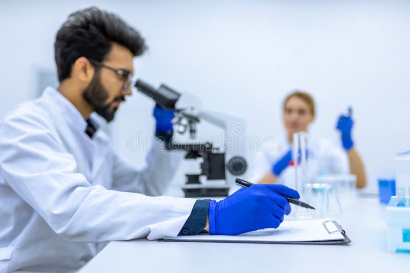αρσενικός επιστήμονας που εργάζεται σε ομάδα ιατρών μικροσκοπίου στο εργαστήριο κάνοντας έρευνα για την πραγματοποίηση σημειώσεων στοκ φωτογραφίες