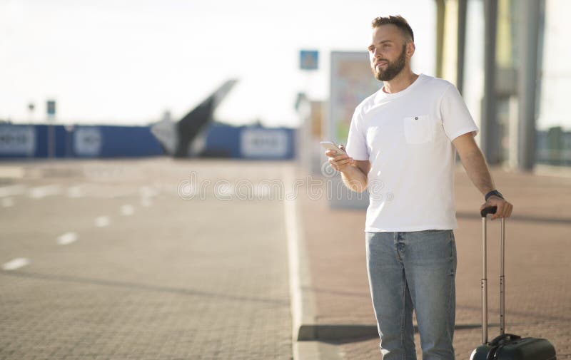 Male tourist arriving at airport, ordering taxi by phone and standing with baggage, free space. Male tourist arriving at airport, ordering taxi by phone and standing with baggage, free space