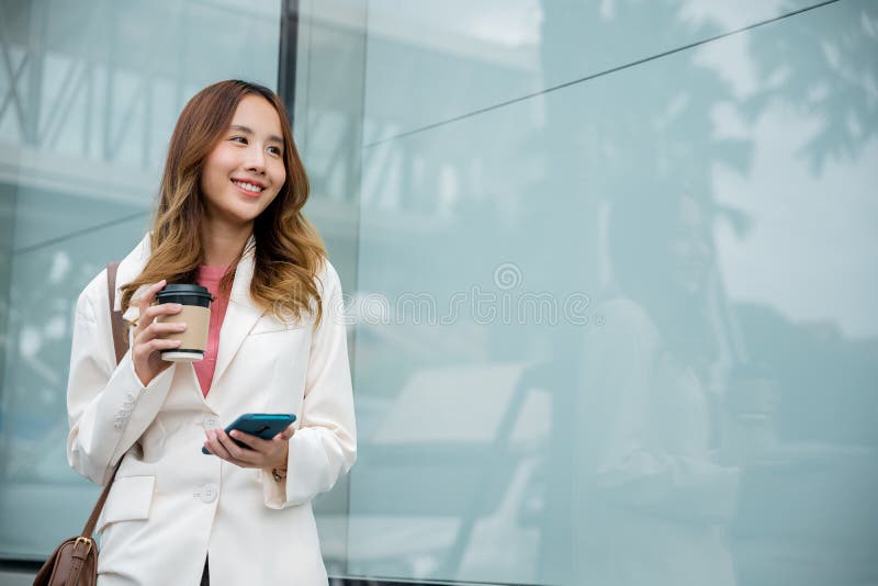 ασιάτισσα επιχειρηματίας με smartphone και καφέ μπροστά στο κτίριο του δρόμου κοντά στο γραφείο στοκ εικόνες