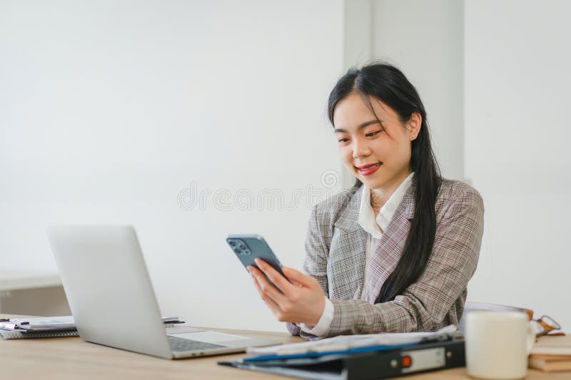 Asian businesswoman happy and cheerful while using smartphones and working. Young businesswoman using apps on cell phones, reading news. Asian businesswoman happy and cheerful while using smartphones and working. Young businesswoman using apps on cell phones, reading news