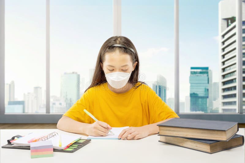 ασιάτισσα κοριτσάκι που φοράει τη μάσκα και κάνει τα μαθήματά της στο σπίτι
