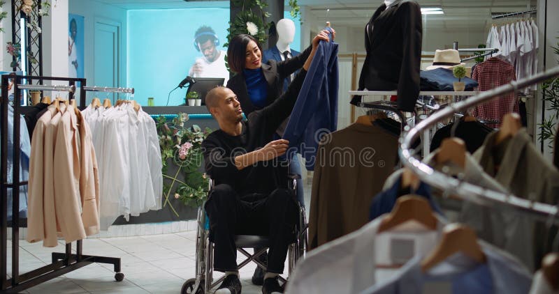 Ασιάτισσα που βοηθάει τους χρήστες αναπηρικών αμαξιδίων να επιλέξουν τα καλύτερα είδη ένδυσης στοκ εικόνες