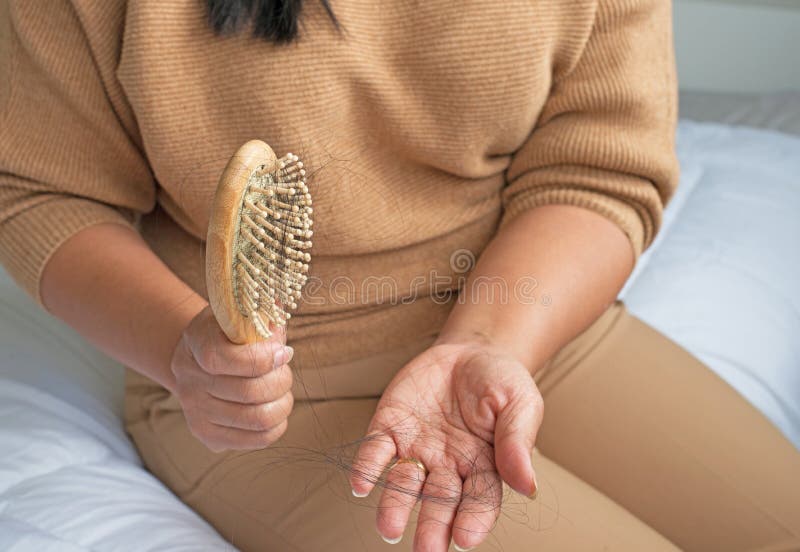 Asian girl sitting in bed holding hairbrush with many hairs, hair loss problems in women causes by hormone balances and stress in any age. Asian girl sitting in bed holding hairbrush with many hairs, hair loss problems in women causes by hormone balances and stress in any age.