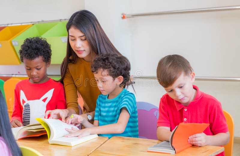 Asian female teacher teaching diversity kids reading book in classroom,Kindergarten pre school concept. Asian female teacher teaching diversity kids reading book in classroom,Kindergarten pre school concept