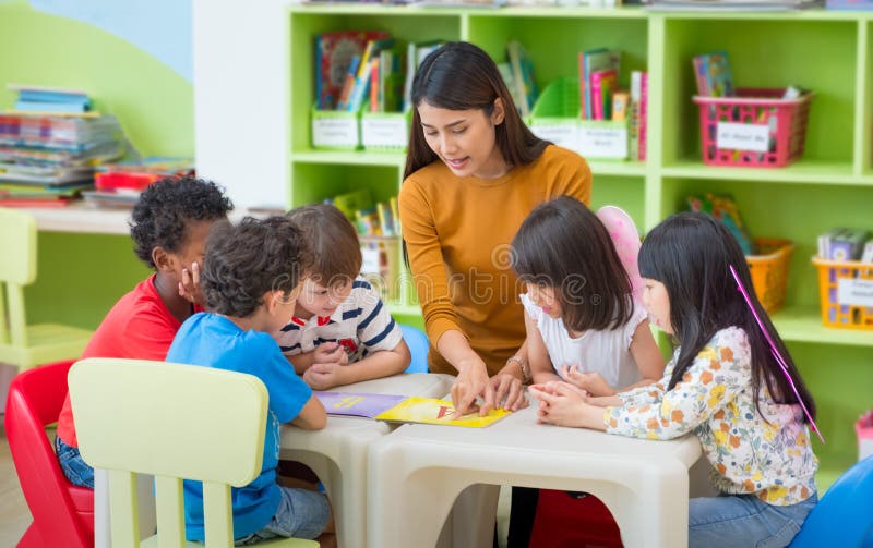 Asian female teacher teaching mixed race kids reading book in classroom,Kindergarten pre school concept. Asian female teacher teaching mixed race kids reading book in classroom,Kindergarten pre school concept