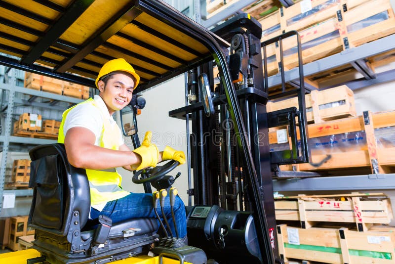 Asian fork lift truck driver lifting pallet in storage warehouse. Asian fork lift truck driver lifting pallet in storage warehouse