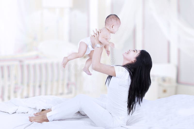 Asian women in bedroom lifting a baby into the air. Asian women in bedroom lifting a baby into the air