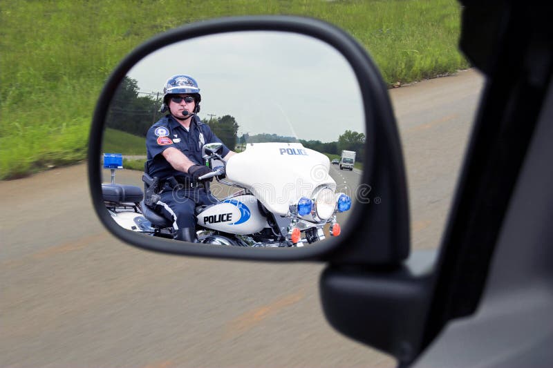 Police officer on his motorcycle watching for speeders is pulling in behind fast moving vehicle. Police officer on his motorcycle watching for speeders is pulling in behind fast moving vehicle