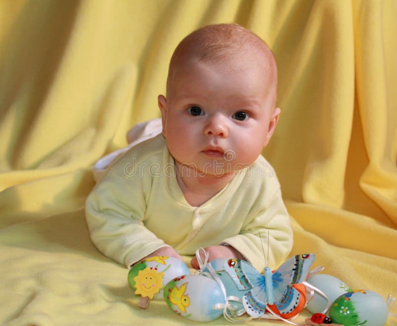 Infant baby boy with artificial Easter eggs on yellow drapery background. Infant baby boy with artificial Easter eggs on yellow drapery background.