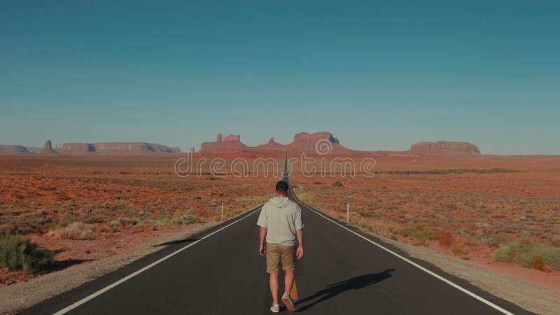 αφηρημένος κινηματογραφιστής άνδρας που περπατά μακριά σε μια ευθεία λεωφόρο ερήμου σε επική ηλιόλουστη τοποθεσία στην κοιλάδα των