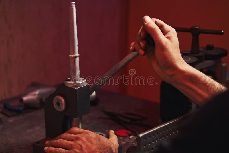 Person lowering the lever of a machine for shaping and forming the ring, situated on mandrel. Person lowering the lever of a machine for shaping and forming the ring, situated on mandrel