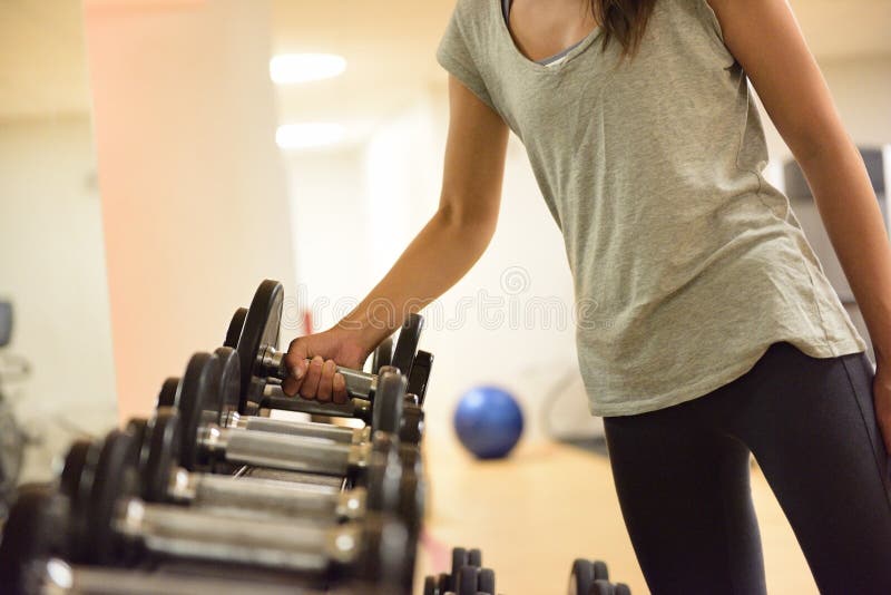 Gym woman strength training lifting dumbbell weights getting ready for exercise workout. Female fitness girl exercising indoor in fitness center. Beautiful fit mixed race Asian Caucasian model. Gym woman strength training lifting dumbbell weights getting ready for exercise workout. Female fitness girl exercising indoor in fitness center. Beautiful fit mixed race Asian Caucasian model.