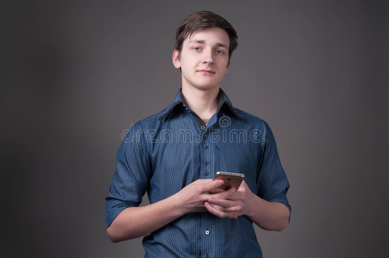 Βέβαιος όμορφος νεαρός άνδρας στο μπλε smartphone εκμετάλλευσης πουκάμισων και εξέταση τη κάμερα στοκ φωτογραφία Βέβαιος όμορφος νεαρός άνδρας στο μπλε smartphone εκμετάλλευσης πουκάμισων και εξέταση τη κάμερα στοκ φωτογραφία
