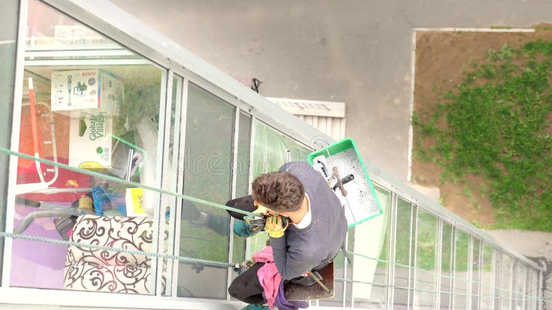 βίντεο ορειβάτη άνδρας πλένει παράθυρα σε πολυόροφο κτίριο. επικίνδυνο επάγγελμα. νεαρός άνδρας εργάζεται ρούχα