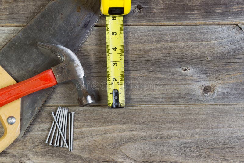 Top view of home repair tools consisting of wood saw, hammer, nails, and tape measure on rustic wooden boards. Top view of home repair tools consisting of wood saw, hammer, nails, and tape measure on rustic wooden boards