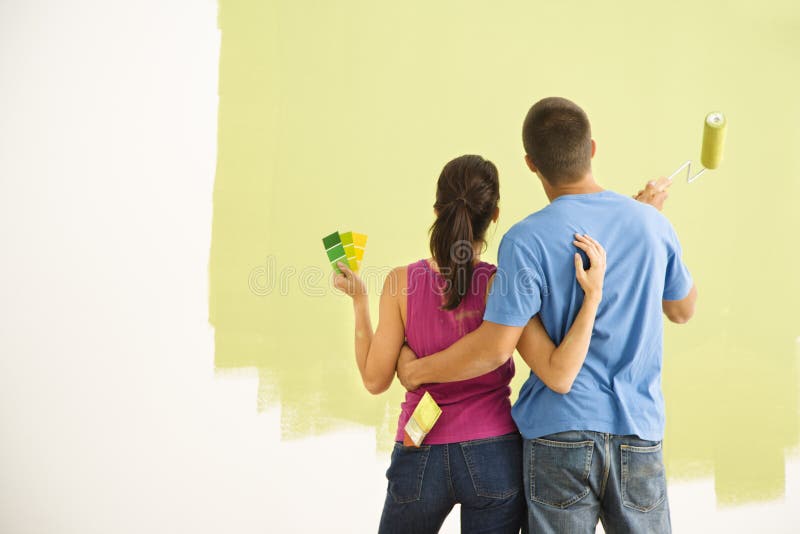 Attractive couple standing in front of partially painted wall with arms around eachother. Attractive couple standing in front of partially painted wall with arms around eachother.