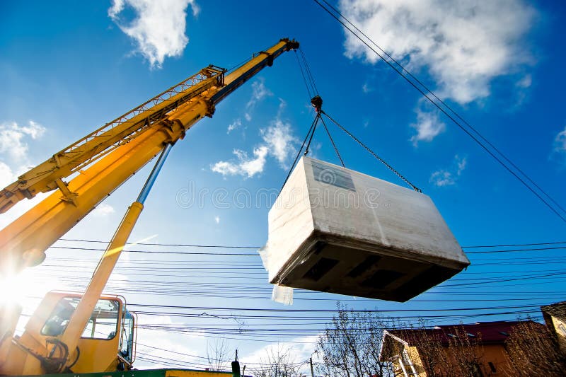 Industrial Crane operating and lifting an electric generator against sunlight and blue sky. Industrial Crane operating and lifting an electric generator against sunlight and blue sky