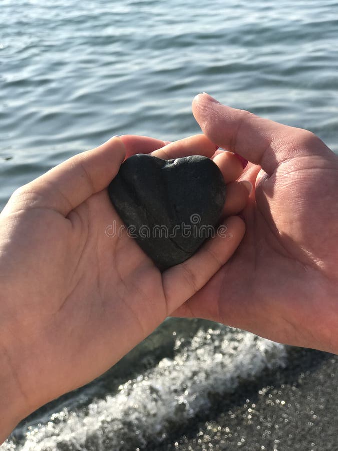 Two hands man and woman holding a heart formed stone on seacoast with wave and sunny day view life goals couple family lucky,  st valentines day, in love, heartbeat, lovestone, i love you. Two hands man and woman holding a heart formed stone on seacoast with wave and sunny day view life goals couple family lucky,  st valentines day, in love, heartbeat, lovestone, i love you