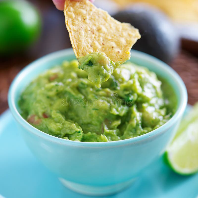 Dipping tortilla chip in mexican guacamole with selective focus on tip of tortilla chip. Dipping tortilla chip in mexican guacamole with selective focus on tip of tortilla chip.
