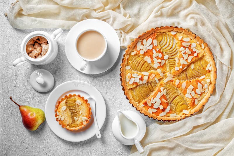 French Pear Tart, La Tarte Bourdaloue filled with poached pears and frangipane cream served on a concrete table with a cup of  cocoa drink and fresh cream, flatlay. French Pear Tart, La Tarte Bourdaloue filled with poached pears and frangipane cream served on a concrete table with a cup of  cocoa drink and fresh cream, flatlay