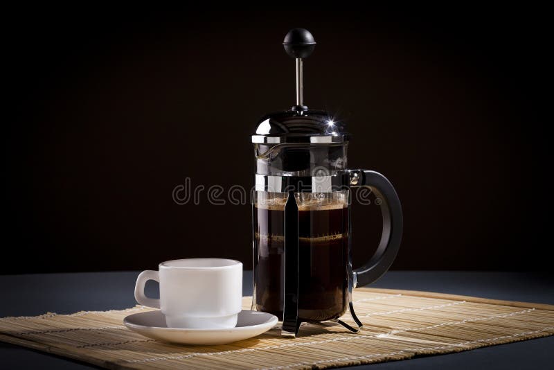 French press coffee maker and coffee cup studio lit on table with dark background. French press coffee maker and coffee cup studio lit on table with dark background