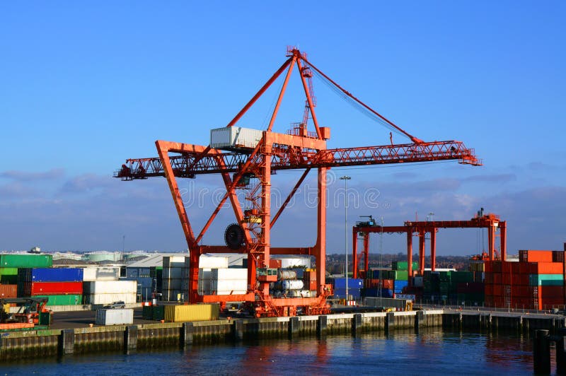 A large red container loading crane surrounded by stacks of different colored containers on the quayside at Dublin Port, Ireland. A large red container loading crane surrounded by stacks of different colored containers on the quayside at Dublin Port, Ireland.