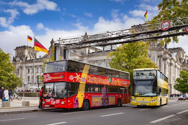 22 September 2018: Berlin, Germany - Tourist double decker buses near The Reichstag, the German parliament building, German flags flying. 22 September 2018: Berlin, Germany - Tourist double decker buses near The Reichstag, the German parliament building, German flags flying.