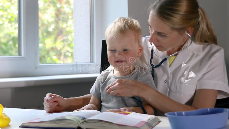 γιατρός που εξετάζει ένα παιδί ασθενή με στηθοσκόπιο ενώ παρακολουθεί το βιβλίο μαζί. χαριτωμένο αγόρι σε παιδιατρικό ραντεβού