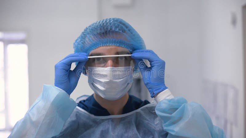 Γιατρός που φορά τα γυαλιά, τη χειρουργικά μάσκα και τα γάντια
