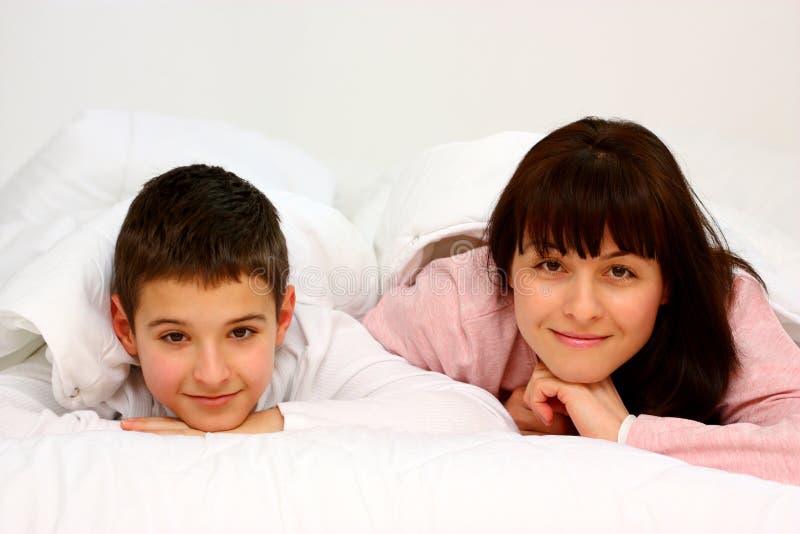 Mother and son in bed smiling covered with white blanket. Mother and son in bed smiling covered with white blanket