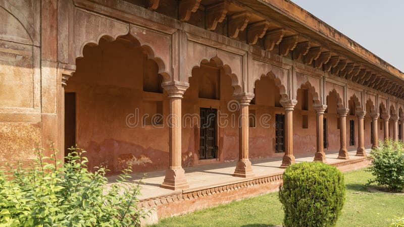 Gallery in the Taj Mahal complex. Terrace, columns, arches made of red sandstone. Wooden doors at the entrance to the premises. Green bushes on the lawn. India. Agra. Gallery in the Taj Mahal complex. Terrace, columns, arches made of red sandstone. Wooden doors at the entrance to the premises. Green bushes on the lawn. India. Agra