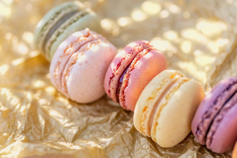 Γλυκά γαλλικά χρωματισμένα macaroons σε χρυσό χαρτί και έναν ξύλινο πίνακα Εύγευστα γλυκά για το τσάι στοκ φωτογραφίες Γλυκά γαλλικά χρωματισμένα macaroons σε χρυσό χαρτί και έναν ξύλινο πίνακα Εύγευστα γλυκά για το τσάι στοκ φωτογραφίες