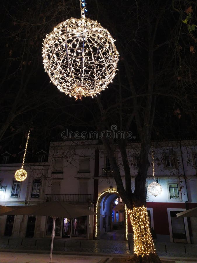 Γοητευτική νυχτερινή σκηνή μιας γοητευτικής πλατείας πόλης, διακοσμημένη με λαμπερά σφαιρικά φώτα κρεμασμένα από τα δέντρα που δημ στοκ εικόνα