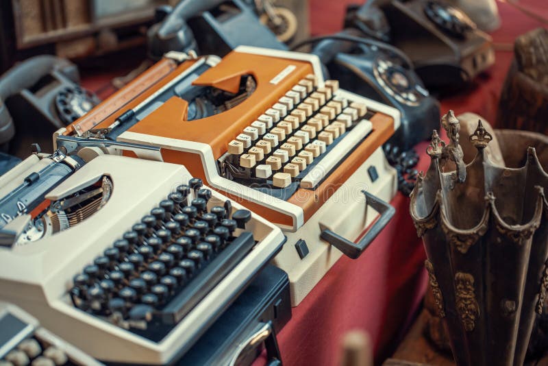 Typewriters from 80`s or 90`s, old telephones and old umbrella stand on the countertop in sunday flea market. Antique bazaar detail. Typewriters from 80`s or 90`s, old telephones and old umbrella stand on the countertop in sunday flea market. Antique bazaar detail