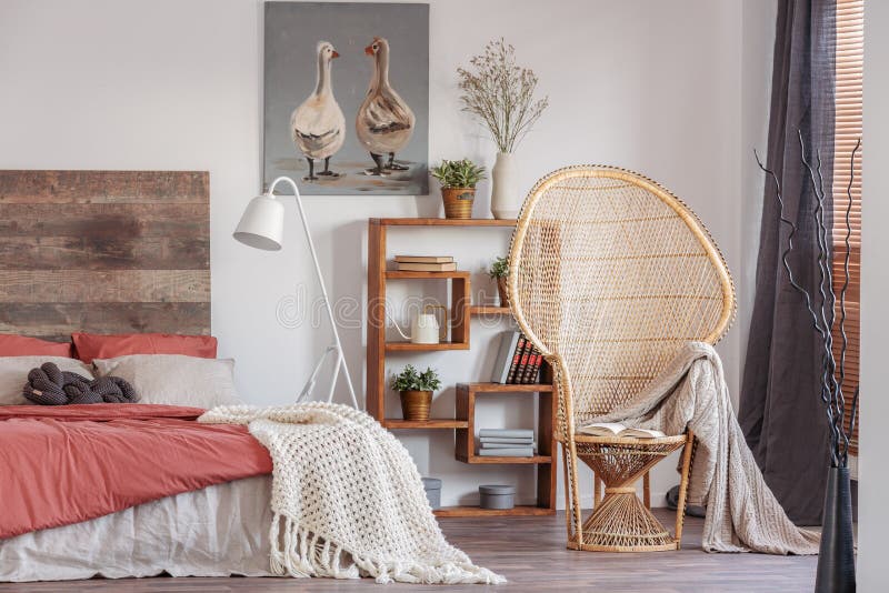 Wicker peacock chair with blanket in fashionable rustic bedroom with bookshelf and bed with bedhead. Wicker peacock chair with blanket in fashionable rustic bedroom with bookshelf and bed with bedhead