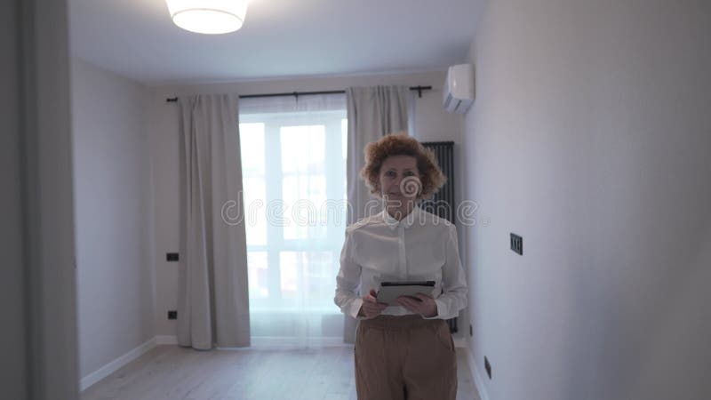 γυναίκα επιχειρηματικού στυλ με λευκό πουκάμισο χαμογελά και κάνει την παρουσίαση του διαμερίσματος για ενοικίαση μόνη της στο απλ φιλμ μικρού μήκους