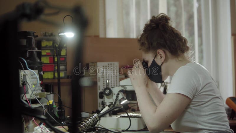 γυναίκα εργαζόμενη σε κέντρο εξυπηρέτησης με μικροσκόπιο και σε συμβούλιο κυκλωμάτων ηλεκτρονικών. κορίτσι που ψάχνει μέσα από μικ
