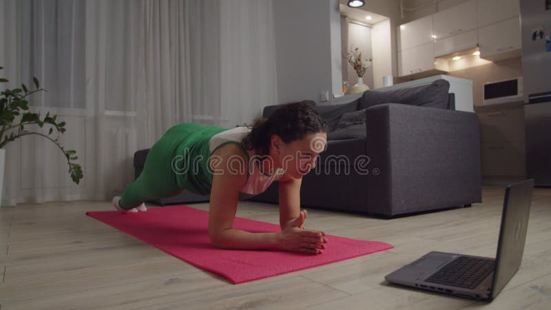 γυναίκα με αθλητική στολή που κάνει γυμναστική με τη χρήση φορητού υπολογιστή στο σπίτι