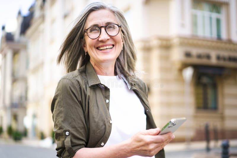 A woman wearing glasses is holding a cell phone in her hand. A woman wearing glasses is holding a cell phone in her hand.