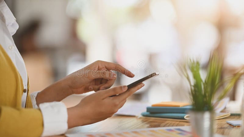 γυναίκα με κίτρινη στολή, με σταυρωμένα τα χέρια στο smartphone, ενώ κάθεται στο σύγχρονο γραφείο εργασίας. στοκ εικόνες