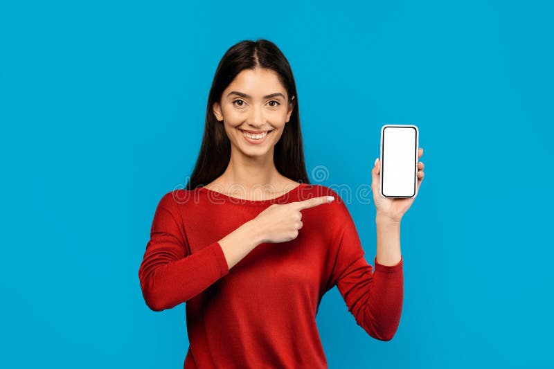 Woman in Red Shirt Holding Smart Phone And Pointing At Blank Screen, Happy Female Demonstrating App Mockup, Standing On Blue Background. Woman in Red Shirt Holding Smart Phone And Pointing At Blank Screen, Happy Female Demonstrating App Mockup, Standing On Blue Background