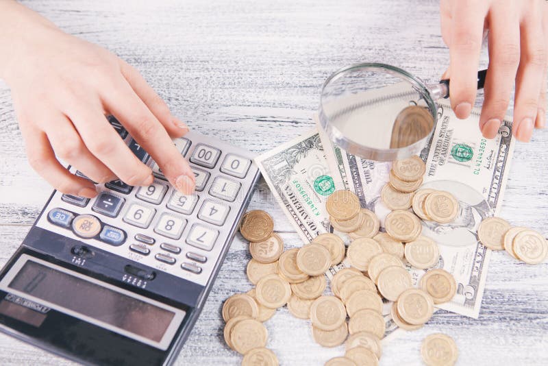 γυναίκα μετράει χρήματα με αριθμομηχανή και φαίνεται με μεγεθυντικό φακό στοκ εικόνα