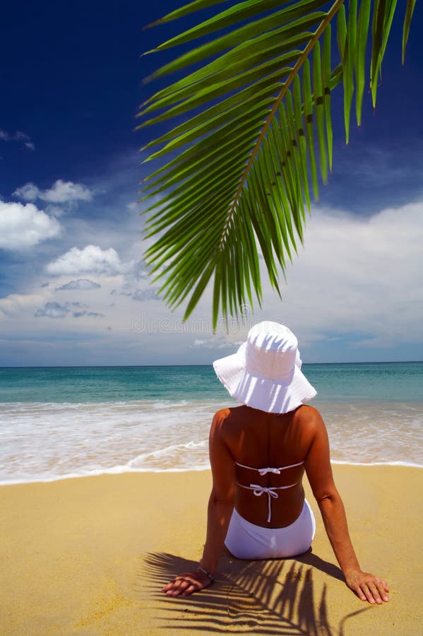 View of nice woman lounging on tropical beach in white panama and bikini. View of nice woman lounging on tropical beach in white panama and bikini