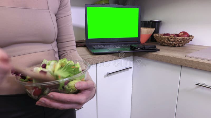 Γυναίκα που αναμιγνύει τις σαλάτες στο κύπελλο κοντά επάνω κοντά στο PC lap-top με την πράσινη οθόνη