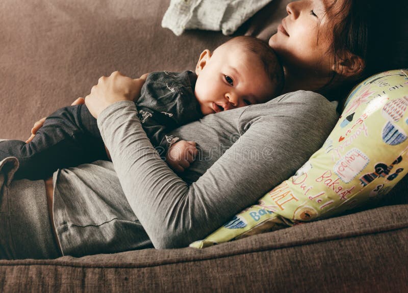 Γυναίκα που βρίσκεται στον καναπέ με τις προσοχές ιδιαίτερες κράτημα του μωρού της