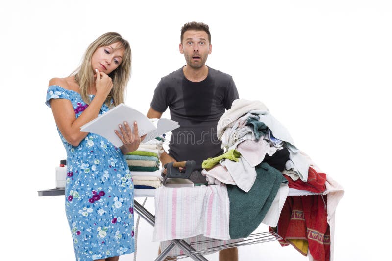 Woman reading a newspaper, while a men shocked and sweating to iron a pile of towels placed on a ironing board. Woman reading a newspaper, while a men shocked and sweating to iron a pile of towels placed on a ironing board