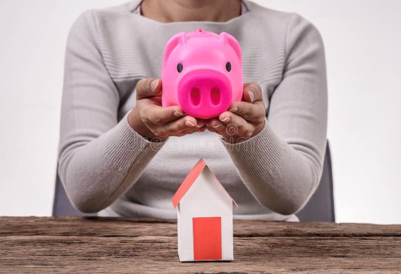 Γυναίκα που κρατά τη piggy τράπεζα και το πρότυπο σπίτι στοκ εικόνες Γυναίκα που κρατά τη piggy τράπεζα και το πρότυπο σπίτι στοκ εικόνες