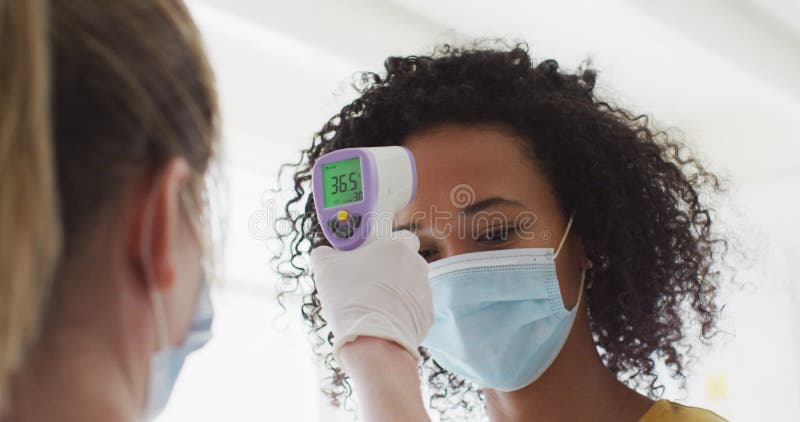 γυναίκα που φοράει μάσκα προσώπου μετρώντας τη θερμοκρασία της στο γραφείο